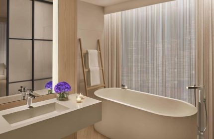 Bathroom at The Times Square EDITION, a most-booked gay luxury hotel in New York's gayborhood. Bathtub, sink, and city view.