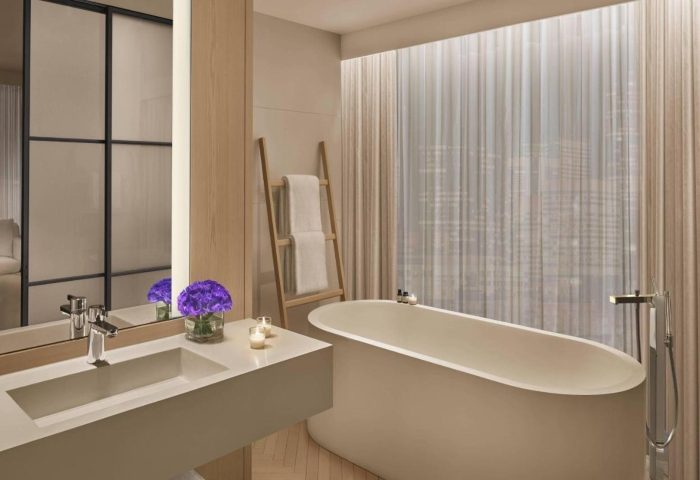 Bathroom at The Times Square EDITION, a most-booked gay luxury hotel in New York's gayborhood. Bathtub, sink, and city view.