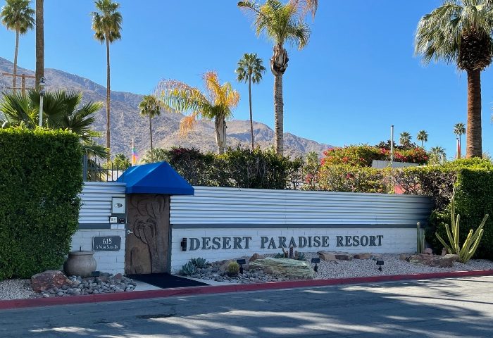 Desert Paradise Resort, a gay men-only hotel in Palm Springs. Entrance with palm trees and mountain backdrop. Gay travel destination.
