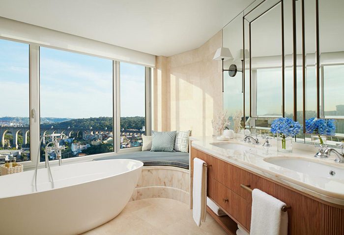 Corinthia Hotel Lisbon honeymoon suite bathroom. Luxury hotel for gay couples, featuring a bathtub, large window, and double sink vanity.