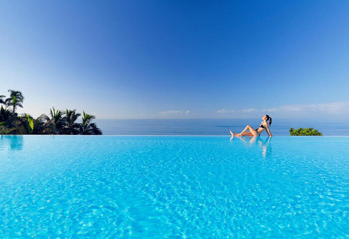 H10 Playa Meloneras Palace rooftop pool. Luxury gay hotel in Gran Canaria. Woman relaxing by the infinity pool overlooking the ocean.