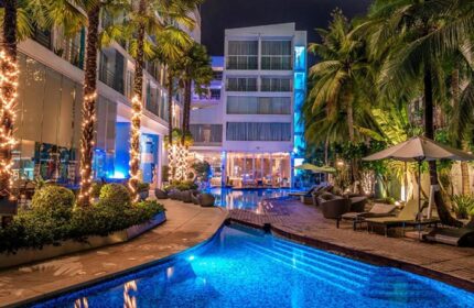 Baraquda Pattaya Mgallery: Luxury gay hotel pool at night. Palm trees, blue lighting, and lounge chairs near gay bars in Pattaya, Thailand.
