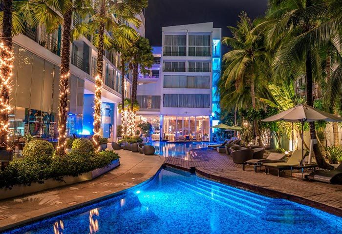 Baraquda Pattaya Mgallery: Luxury gay hotel pool at night. Palm trees, blue lighting, and lounge chairs near gay bars in Pattaya, Thailand.