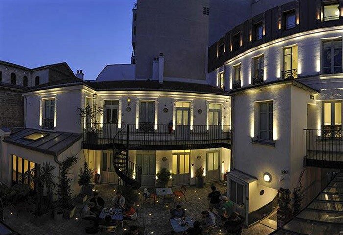 The 3 Ducks Eiffel Tower by Hiphophostels courtyard at night. Party hostel near Paris with gay nightlife, outdoor seating, and spiral staircase.