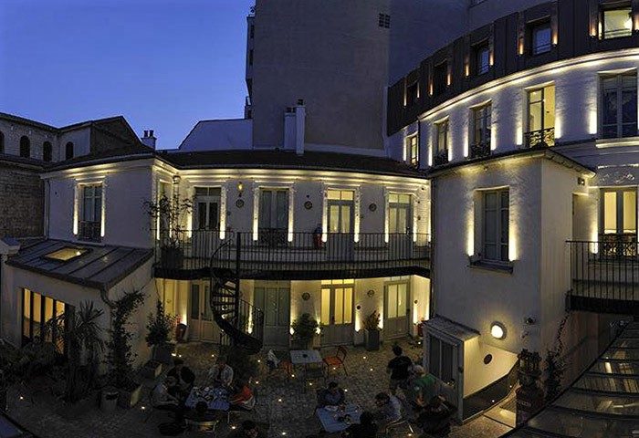 The 3 Ducks Eiffel Tower by Hiphophostels courtyard at night. Party hostel near Paris with gay nightlife, outdoor seating, and spiral staircase.