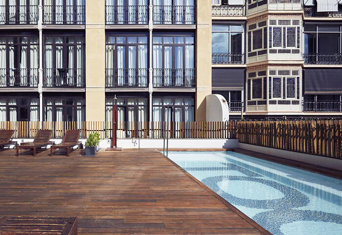 TOC Hostel Barcelona pool. Most gay popular hostel in Barcelona city center. Wooden deck, lounge chairs, and building facade.