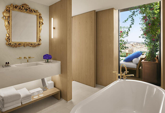 Bathroom at The Barcelona EDITION, a gay-popular hotel in Barcelona's gayborhood. Features a tub, balcony with city views, and ornate mirror.