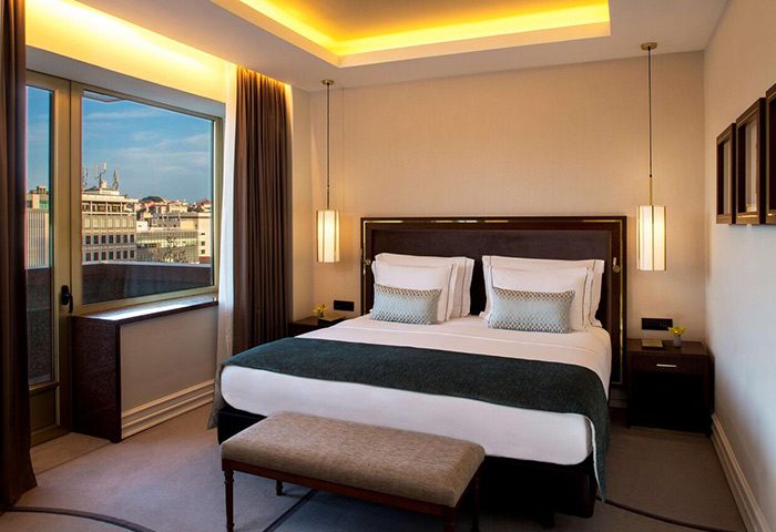 Tivoli Avenida Liberdade luxury hotel room in Lisbon's gayborhood. Upscale gay travel lodging with city view, bed, bench, and stylish lighting.