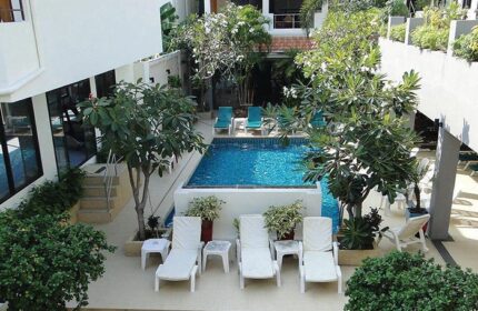 Sansuk Sauna Guesthouse in Pattaya. Adults-only gay hotel with pool. View of the pool area with sun loungers, plants, and trees.