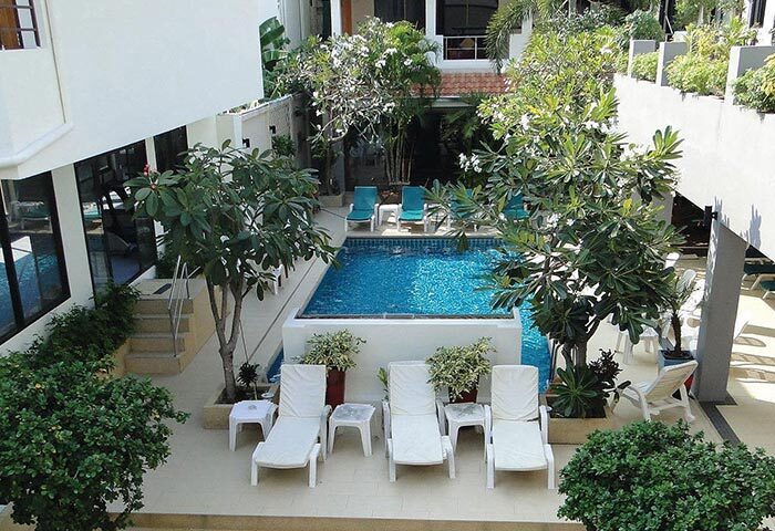 Sansuk Sauna Guesthouse in Pattaya. Adults-only gay hotel with pool. View of the pool area with sun loungers, plants, and trees.