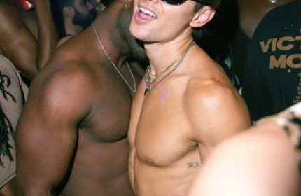 Gay New York: Men dancing shirtless at The Rosemont, a popular gay bar in NYC. A man in sunglasses smiles at the camera. Nightlife scene.