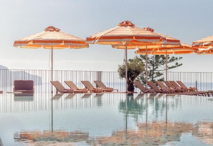 NEXT Hotel Madeira pool view. Striped umbrellas and loungers reflect in the water. A popular gay beach hotel for young gay travelers in Portugal.