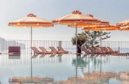 NEXT Hotel Madeira pool view. Striped umbrellas and loungers reflect in the water. A popular gay beach hotel for young gay travelers in Portugal.