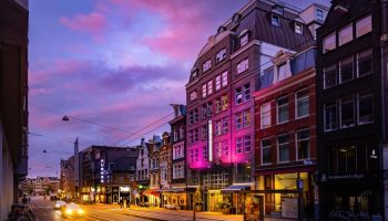Amsterdam's Boutique Hotel Albus at dusk. A popular gay hotel near the canal, lit with pink lights. A vibrant, welcoming scene.