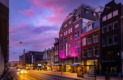 Amsterdam's Boutique Hotel Albus at dusk. A popular gay hotel near the canal, lit with pink lights. A vibrant, welcoming scene.