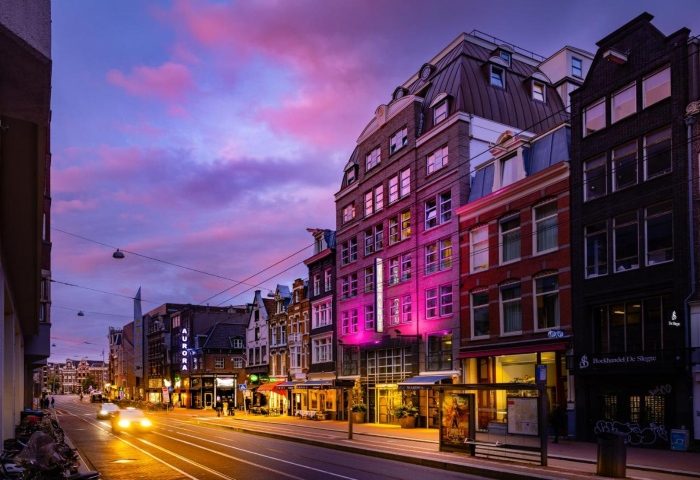 Amsterdam's Boutique Hotel Albus at dusk. A popular gay hotel near the canal, lit with pink lights. A vibrant, welcoming scene.