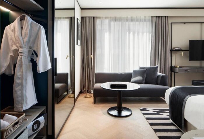 Academias Hotel, Athens, Autograph Collection room. Modern interior: robe, sofa, table, TV, safe. Gay-friendly hotel location for travel advice.