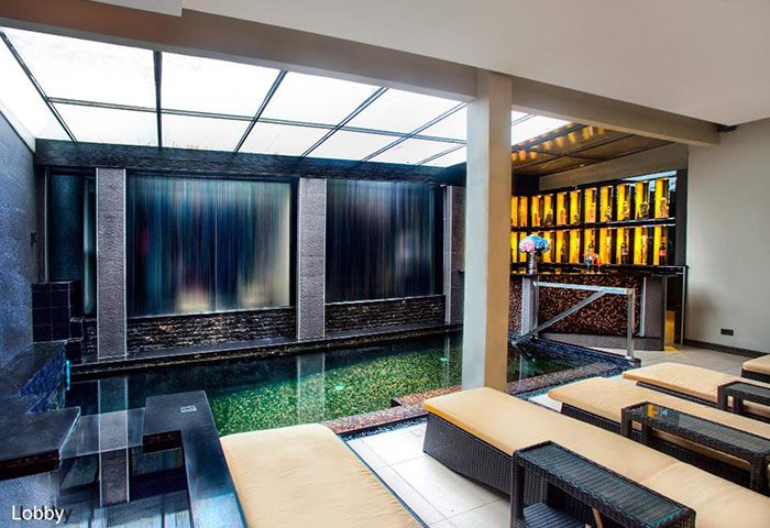 Poseidon Boutique Hotel's pool area in Pattaya, Thailand. Gay hotel with lounge chairs, bar, and waterfall feature near Jomtien Beach.