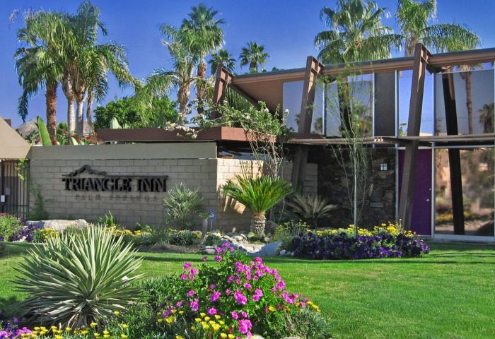 Triangle Inn Palm Springs, a popular gay men's hotel. Lush landscaping, modern architecture, and an inviting outdoor space. Palm trees abound.