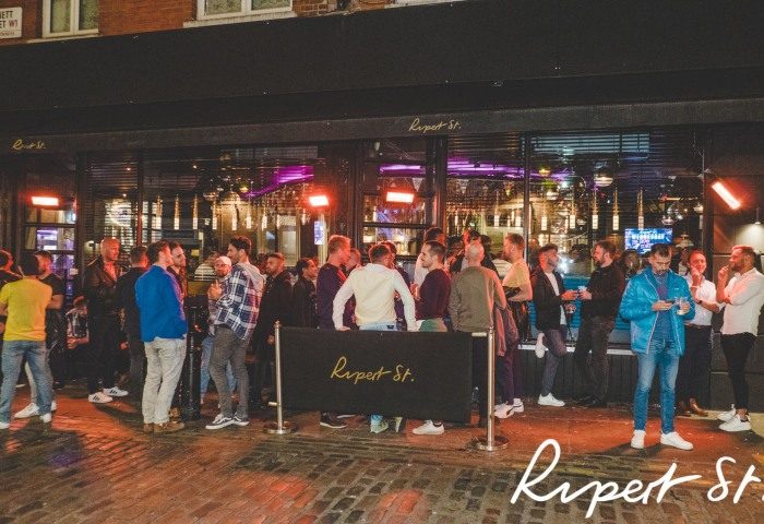 Rupert Street Bar, Soho, London. A popular gay street bar with a crowd of men socializing outside at night. Gay travel advice.