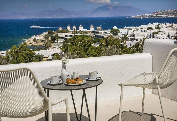 Ilio Maris gay hotel, Mykonos. Balcony view with coffee, croissants, windmills, and ocean. Upscale gay travel near Jackie O Bar.