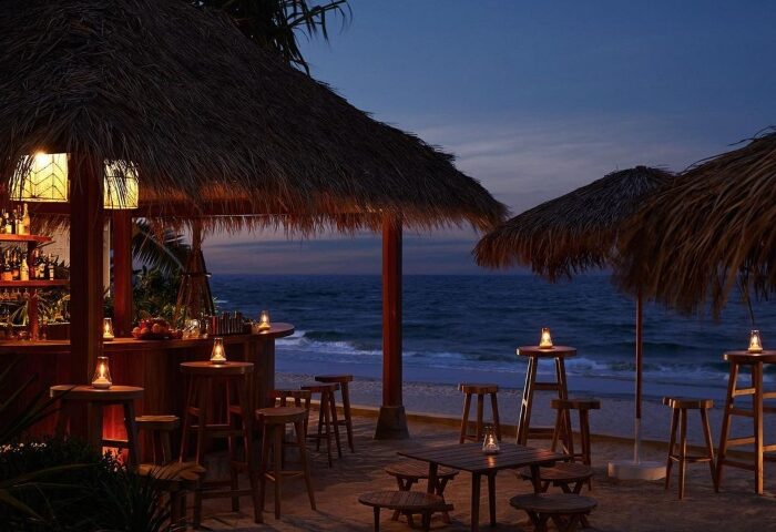 Romantic gay beach resort Hua Hin, The Standard. Beach bar with thatched roof, tables, and chairs at dusk. Perfect for gay travel.