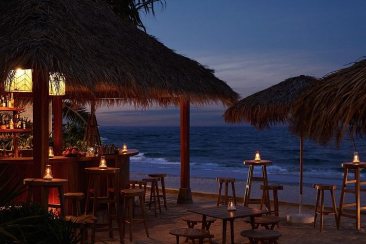 Romantic gay beach resort Hua Hin, The Standard. Beach bar with thatched roof, tables, and chairs at dusk. Perfect for gay travel.
