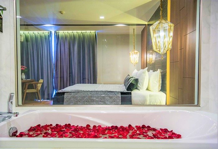 Romantic gay luxury hotel stay in Chiang Mai. Bathtub with rose petals, bedroom with hanging lights, curtains and desk.