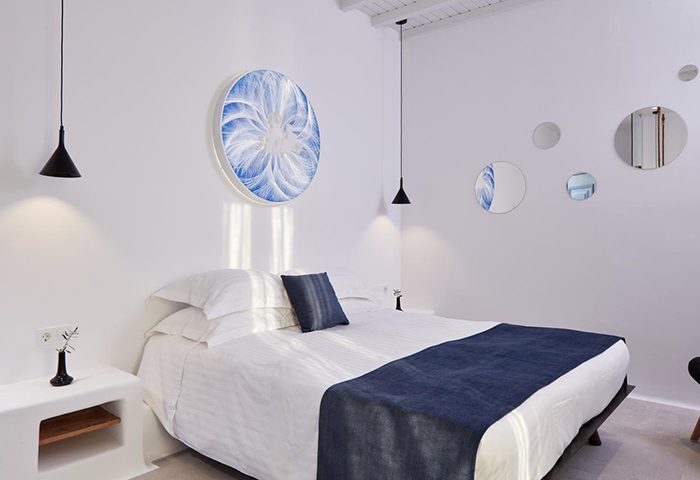 Absolute Mykonos Suites: Stylish luxury gay hotel room. White walls, bed with blue accents, round art, & mirrors. Modern design.