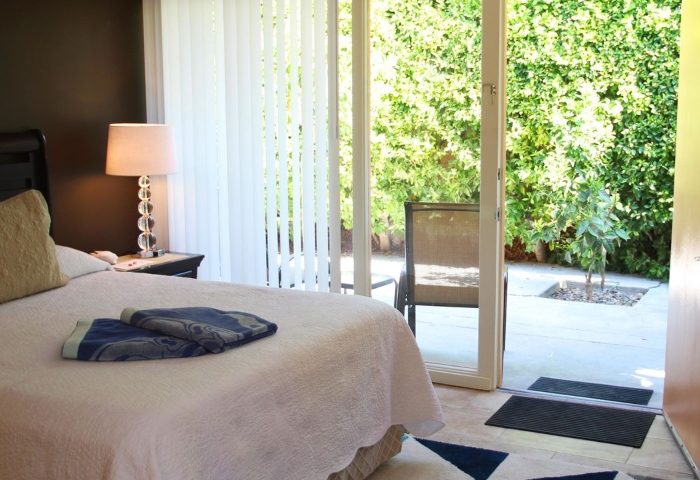 Triangle Inn Palm Springs room with patio. Gay men's hotel featuring garden views, bed, and nightstand. Most-Talk-About hotel for gay travelers.