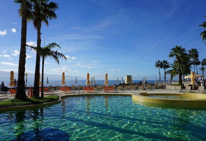 NEXT Hotel Madeira beachfront pool view. Trendy gay hotel in Portugal with palm trees, lounge chairs, and ocean views.