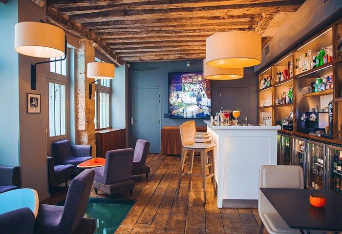 Hotel Jules & Jim, unique gay hotel in Paris. Bar area with wooden floors and ceiling, purple chairs, and a well-stocked bar.