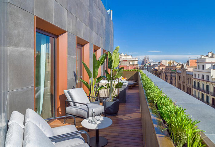 H10 The One Barcelona balcony view. Luxury gay hotel in Barcelona with city views, seating area, and lush greenery. Top choice for gay travelers.