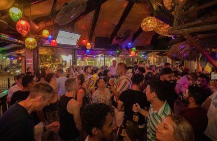 Crowded Mr. Flamingo Gay Bar in Puerto Vallarta, Mexico. People socializing under colorful lights and ceiling fans. Nightlife scene.