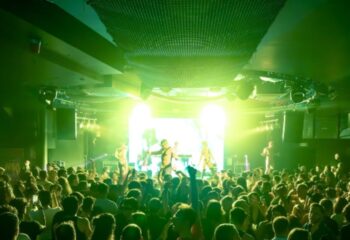 Muccassassina Rome: A vibrant gay club scene with a crowd enjoying the show. Green lights illuminate the stage and dance floor.