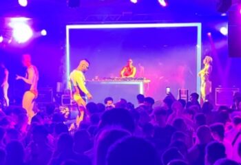 Muccassassina Rome: DJ and dancers perform on stage at a crowded gay party. Purple lighting and energetic atmosphere. Gay travel in Rome.