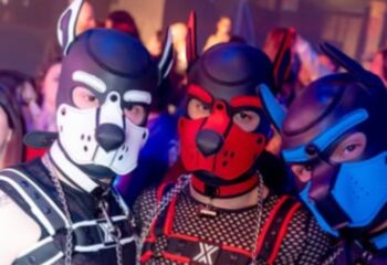 Three men in puppy masks at Muccassassina, Rome's iconic gay party. Leather harnesses, chains, and playful fetish gear add to the vibrant atmosphere.
