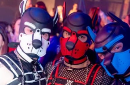 Three men in puppy masks at Muccassassina, Rome's iconic gay party. Leather harnesses, chains, and playful fetish gear add to the vibrant atmosphere.