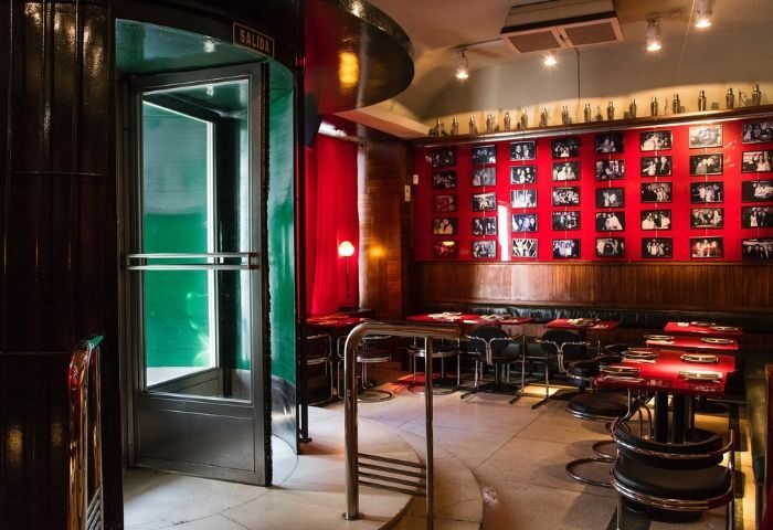Museo Chicote Gay Bar in Madrid. Interior view of the stylish bar with red walls, photos, tables, and a revolving door.
