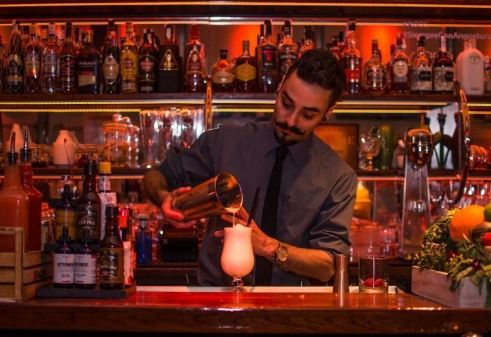Bartender pouring cocktail at Museo Chicote Gay Bar in Madrid. Travel advice for gay men in Spain. Lively nightlife scene.