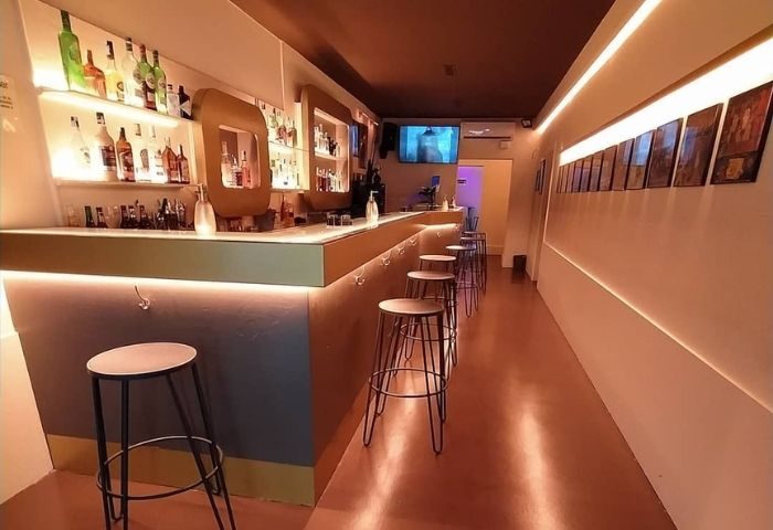 Interior of a gay bar in Barcelona. A long bar with stools, shelves of liquor, and soft lighting. Museum Bar, a popular gay bar.