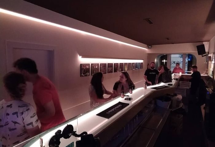 People at a Museum Gay Bar in Barcelona. Patrons sit at the illuminated bar, enjoying drinks and conversation. A popular gay bar.