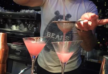 Bartender making pink cocktails at My Bar, Rome. Gay bar with Bears t-shirt. Gay travel advice, nightlife, and Rome's gay scene.