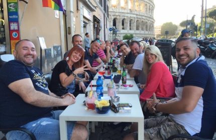 Gay travel: Group of friends at a bar in Rome, Italy, with the Colosseum in the background. Rainbow flag visible. My Bar Rome.