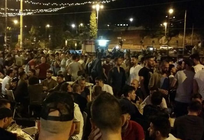 Night view of a crowded gay bar in Rome. Many men are standing and sitting at tables, enjoying the nightlife scene. Gay travel advice.