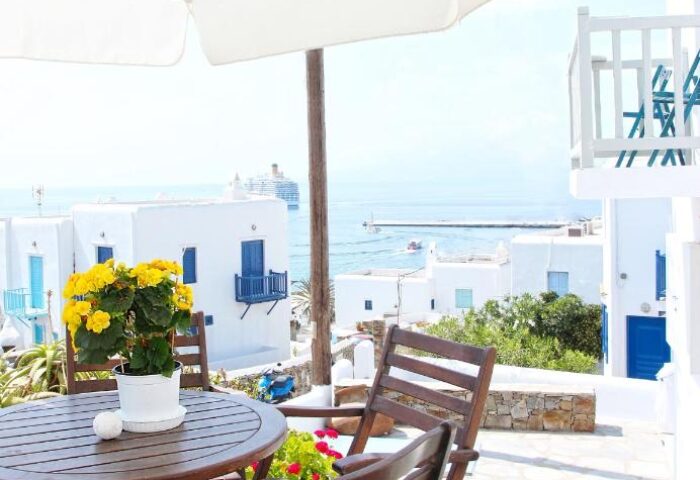 Myconian Inn gay budget hotel patio view. Table, chairs, and flowers overlook the Aegean Sea. A relaxing spot in Mykonos, Greece.