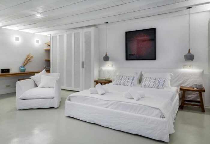 Myconian Inn room. Gay budget hotel with white decor, bed, chair, wardrobe, and art. Mykonos travel for gay men. Minimalist design.