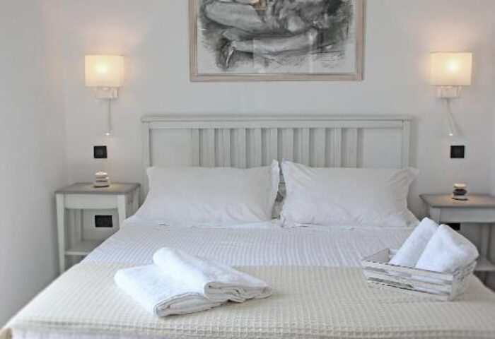 Myconian Inn gay budget hotel room. White interior, double bed, bedside tables, and artwork. Clean, simple design for gay travelers.