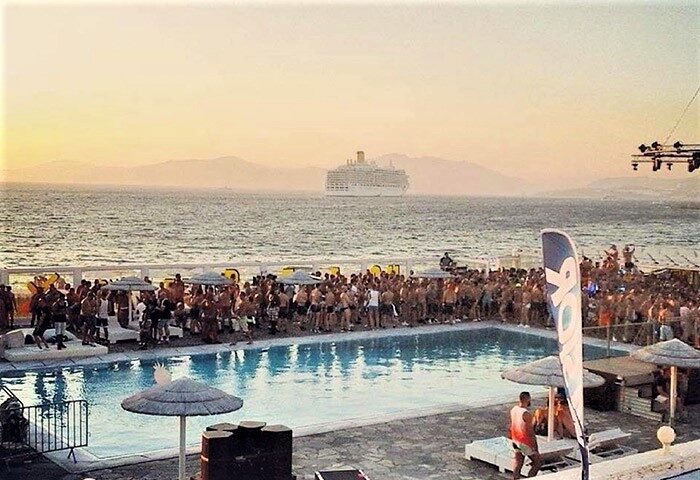 Mykonos Bay Resort & Villas beachfront hotel gay party. Poolside event in Mykonos Town, cruise ship on the sea. Gay travel advice.