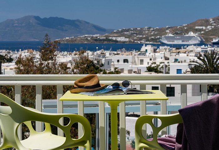 Semeli Hotel Mykonos balcony view. Hat, sunglasses, and magazine on table. Mykonos Town, city center, tourist attractions, gay bars visible.